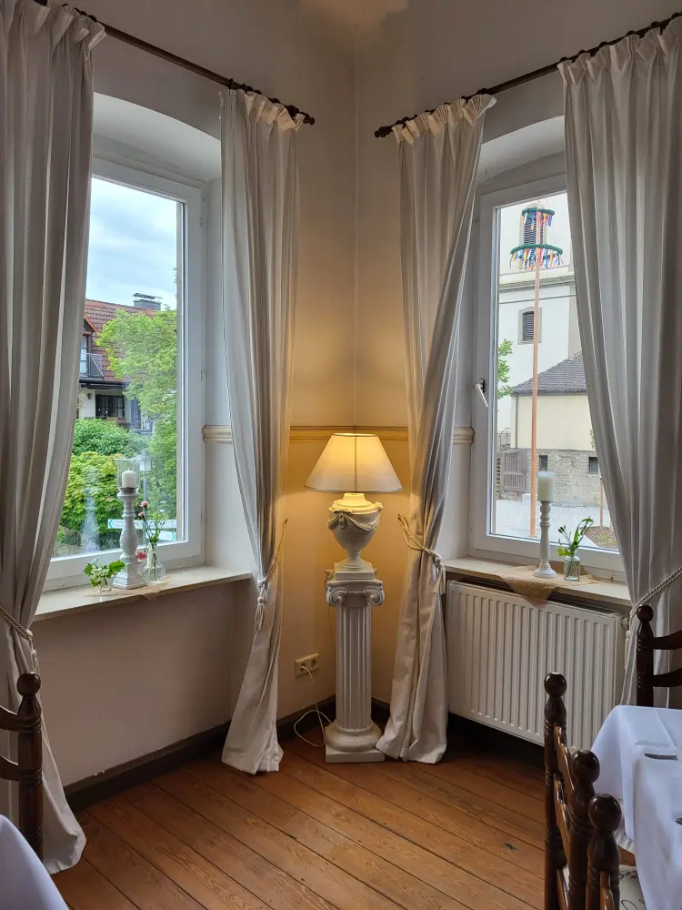 Fensterdekoration mit weißen Vorhängen, einer Stehlampe und einer klassischen Säule in einem eleganten Salon.